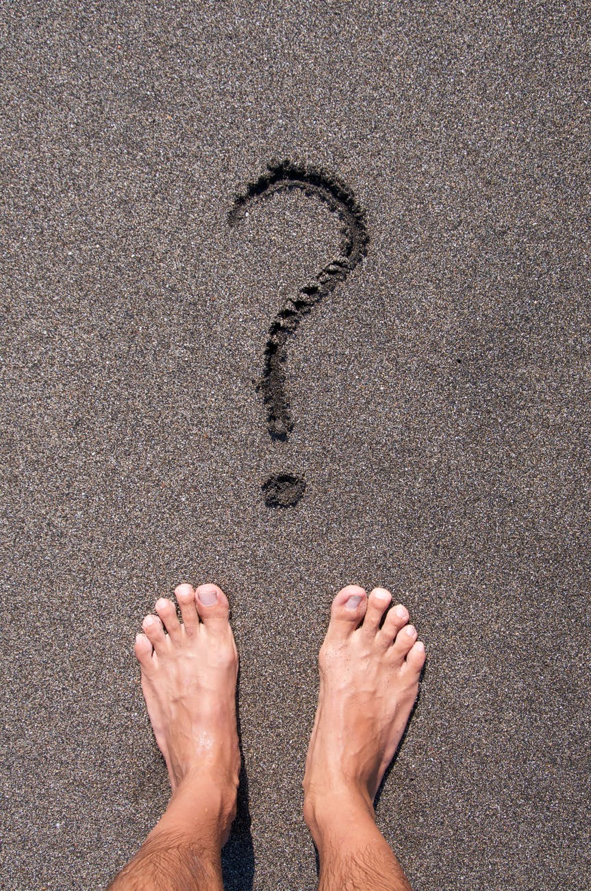 person standing on black sand beach in front of question mark