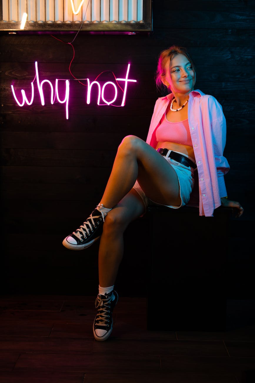 woman in pink blazer and black and white striped mini skirt sitting on brown wooden floor