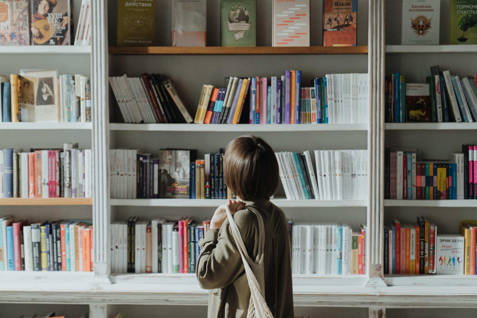 woman in beige coat standing near white wooden book shelf